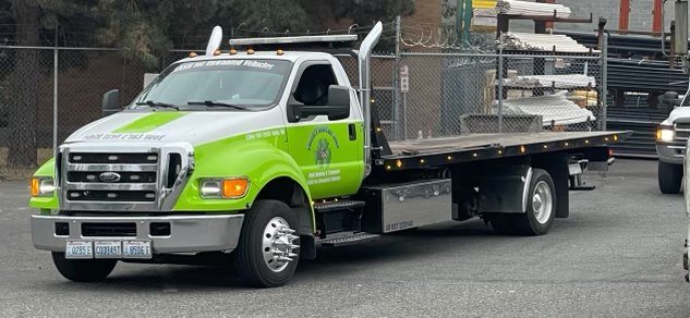 Green flatbed tow truck parked in the salvage yard