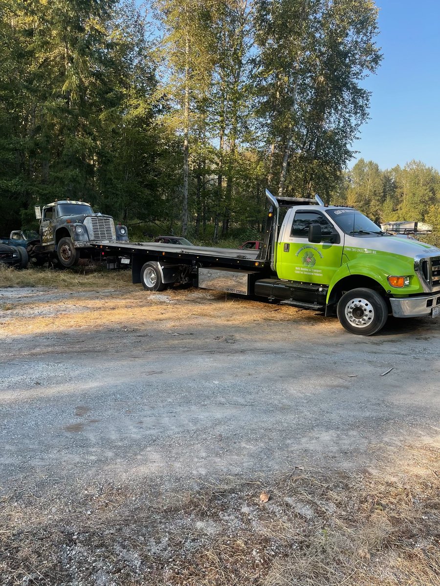 Flatbed tow truck hauling a vintage junk pickup on a rural lot